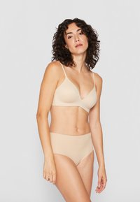 Beige bh en naadloze hoge taille slipset, gemaakt van gladde stof met verstelbare bandjes en een V-hals ontwerp, die een flexibele pasvorm biedt.