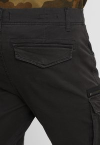 Czarne spodnie cargo z teksturowanej tkaniny, z tylną kieszenią na klapę i boczną kieszenią na zamek, zaprojektowane w slim fit.