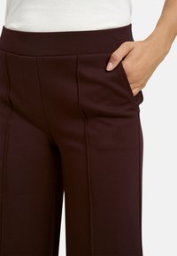 Burgundy wide-leg trousers with a smooth texture, featuring a high waistband and side pocket detail, designed for comfort and a tailored fit.