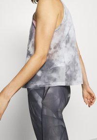 Top in tessuto tie-dye grigio e bianco con design senza maniche, abbinato a leggings scuri con motivo geometrici, che mostrano una vestibilità comoda.