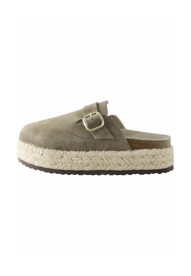 Suedeslipper med bred rem og metalspænde. Har en espadrille-lignende jute-sål og en brun gummibund. Farven er dæmpet grøn.