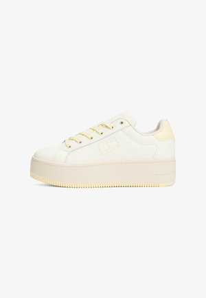 Baskets plates blanches avec un dessus en cuir lisse, accents beiges et lacets jaunes. Présente une semelle texturée et un logo sur le côté.
