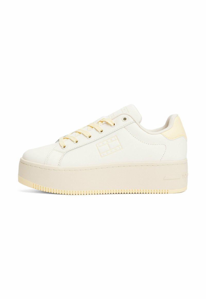 Baskets plates blanches avec un dessus en cuir lisse, accents beiges et lacets jaunes. Présente une semelle texturée et un logo sur le côté.