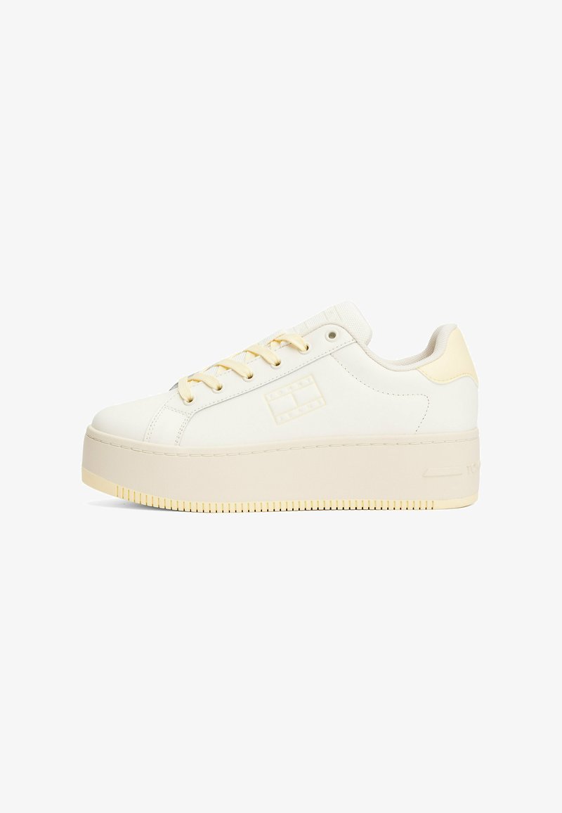 Zapatillas de plataforma blancas con parte superior de cuero suave, acentos en beige y cordones amarillos. Presentan una suela texturizada y un logo en el costado.