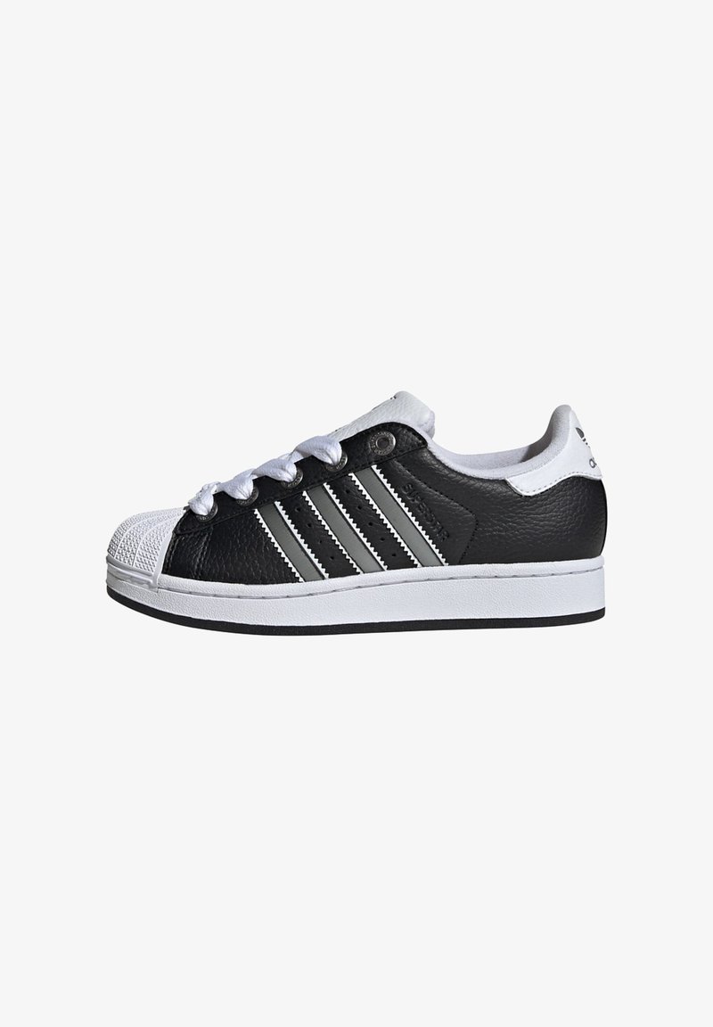 Black and white sneaker with a leather upper, rubber toe cap, three grey stripes on the side, and white laces. Flat sole design.