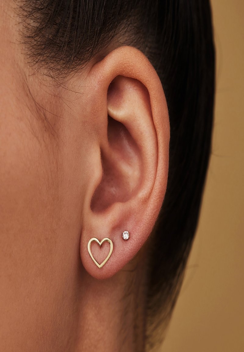 Gros plan d'une oreille droite portant deux boucles d'oreilles : un petit anneau en or en forme de cœur et une petite puce ronde en diamant.