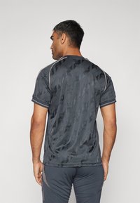 Jersey atlético gris oscuro con un patrón geométrico texturizado, mangas cortas, ribetes contrastantes en el cuello y un diseño ajustado.