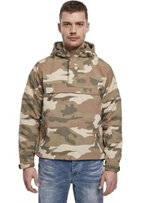 Veste camouflage avec capuche, fabriquée en tissu léger. Présente une poche avant et des poignets élastiques. La palette de couleurs comprend des tons beige et vert.