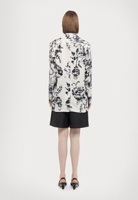 Sort og hvid blazer med blomsterprint og lange ærmer, parret med sorte shorts. Glat stof og let løst fit.