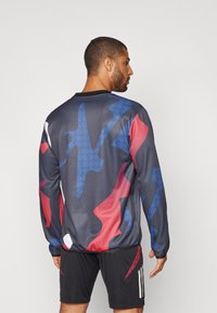 Maglia atletica a maniche lunghe in grigio scuro, con un audace motivo astratto e accenti blu, rossi e bianchi. Realizzata in tessuto traspirante.