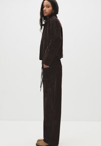 Ruskea corduroypuku ja vastaavat housut rentoa istuvuutta. Asusteessa on kiristysvyötärö, sivutaskut ja silkkinen pinta.