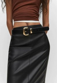 Musta nahkahame, jossa on korkea vyötärö, yhdistetty paksuun mustaan vyöhön, jossa on kultainen suorakulmainen solki. Sileä pinta, tyylikäs muotoilu.