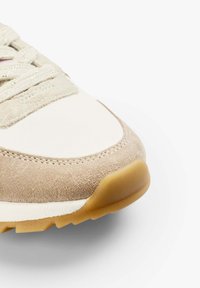 Sneaker with a cream fabric upper and beige suede accents. Features laces, stitched detailing, and a gum rubber outsole.