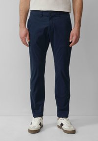 Marineblaue Baumwollchinos mit geradem Schnitt, ausgestattet mit einem vorderen Knopfverschluss und Seitentaschen, kombiniert mit weißen Sneakers.