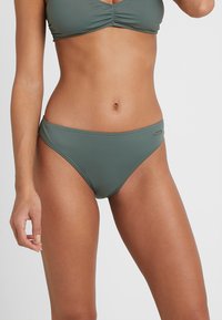 Bikini-Set in gedämpftem Grün, aus glattem, elastischem Stoff gefertigt. Verfügt über ein schlichtes Design mit Raffung oben und minimalem Branding-Detail.