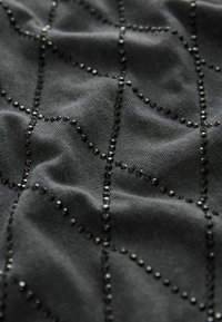 Tessuto nero con una superficie texture, caratterizzato da un motivo a griglia di piccole perle nere che crea contrasto visivo. Texture liscia e morbida.
