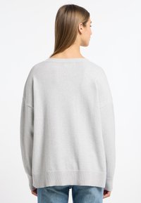 Hellgrauer, oversized Strickpullover mit breitem Rippenbund und Säumen, überschnittenen Schultern und weicher Textur, von hinten betrachtet.