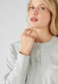 Camicia a maniche lunghe grigia chiaro in tessuto morbido, con scollatura rotonda, tre bottoni e una tasca con pois bianchi e una cucitura a contrasto.