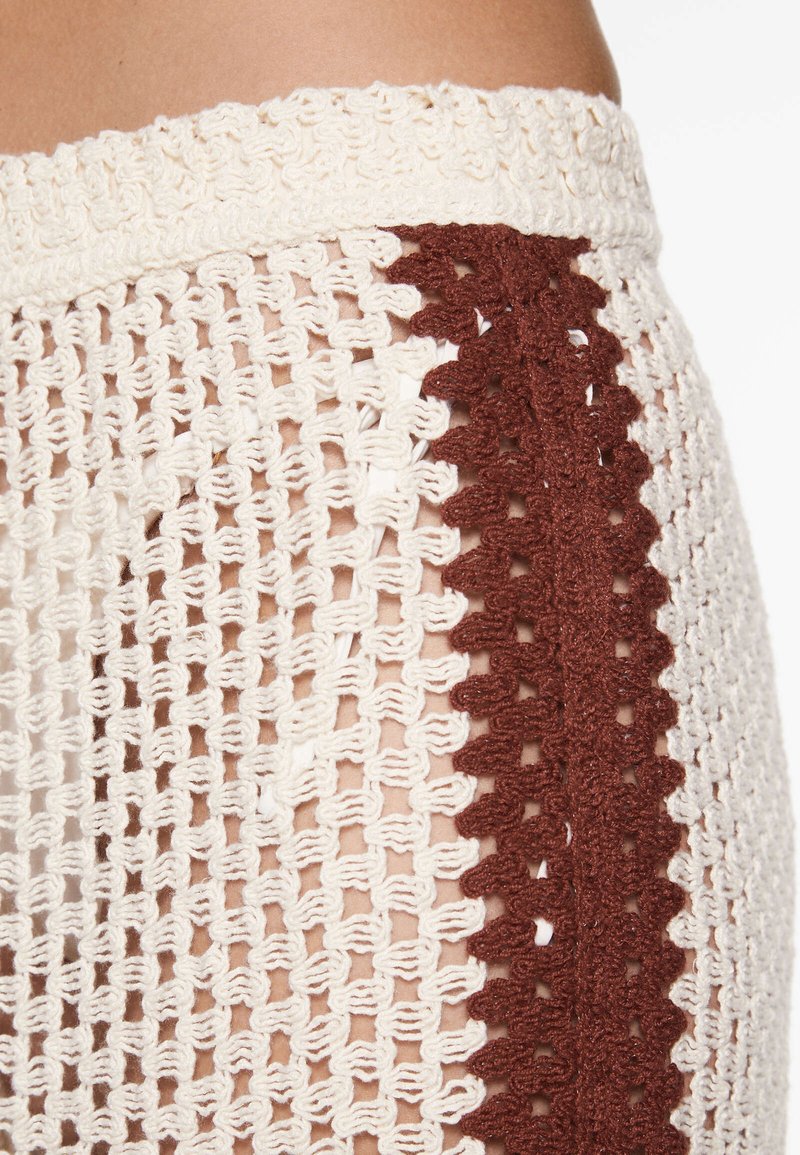 Gonna all'uncinetto con un design a maglia aperta, caratterizzata da un corpo bianco con un accento a zigzag marrone lungo il lato e una vita testurizzata.