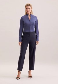 Marineblauwe, op maat gemaakte broek gecombineerd met een lichtblauw, lang mouwig overhemd met knopen. Het overhemd heeft een opstaande kraag en een gladde stoftextuur.