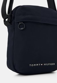 Borsa a tracolla blu navy realizzata in tessuto testurizzato; presenta una tasca frontale, una tracolla in nylon e il dettaglio del logo "TOMMY HILFIGER" in argento.