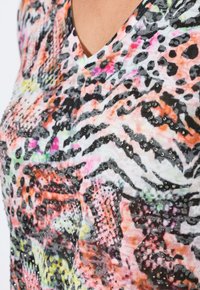 Tričko s výstřihem do V a barevným potiskem zvířat v odstínech oranžové, růžové a černé, zdobené akcenty z rhinestones.