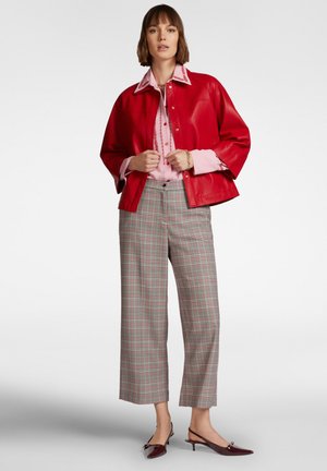 Giacca in ecopelle rossa sopra una blusa rosa con ricami floreali, abbinata a pantaloni a palazzo a quadri e décolleté slingback bordeaux.