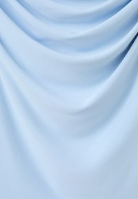 Tissu bleu clair doux et lisse avec de légers plis créant des ombres courbes et des reflets, mettant en valeur sa texture et son drapé.