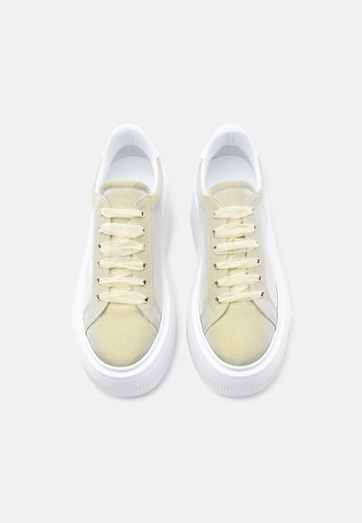 Ζευγάρι από ανοιχτό κίτρινα πάνινα παπούτσια με χοντρές λευκές λαστιχένιες σόλες και κορδόνια στο ίδιο κίτρινο χρώμα, σε λήψη από πάνω πάνω σε λευκό φόντο.