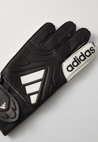 Gant de gardien de but noir en matériau synthétique. Présente une grip texturé, un logo "adidas" blanc et trois rayures blanches diagonales.