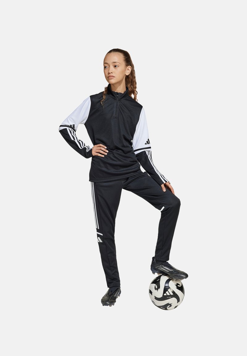 Survêtements de sport noir avec des manches blanches, trois bandes sur les bras et les pantalons, col zippé, design ajusté, associé à un ballon de soccer noir et blanc.