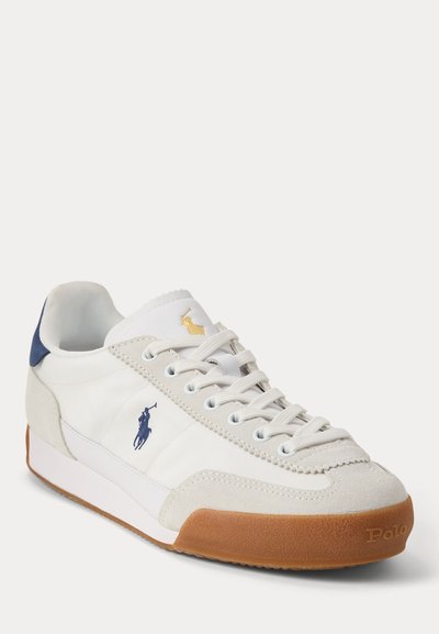 Witte en beige Polo sneaker met bruine zool, donkerblauwe hieltab, veters en Polo-logo aan de zijkant en op de tong.