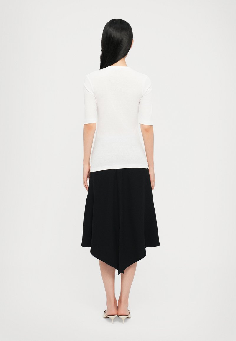 Top bianco aderente con maniche a tre quarti abbinato a una gonnellina nera con orlo asimmetrico. Texture del tessuto liscia.