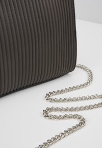 Czarna torebka z żebrowanym wzorem, o teksturowanej powierzchni, z srebrnym łańcuszkiem i eleganckim designem. Gładkie krawędzie i minimalistyczne detale metalowe.