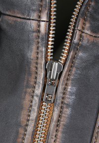 Braunes Leder mit Reißverschlussdetail und sichtbaren Nähten. Silberner Metallreißverschluss mit Zipper und Zähnen, der im Kontrast zur glatten Lederoberfläche steht.