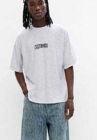 Light grey oversized t-shirt with short sleeves and a printed "STWD" logo. Paired with blue textured jeans featuring vertical stripes.