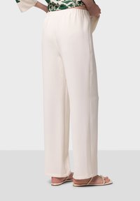Witte, luchtige broeken met een elastische tailleband, met rechte pijpen en minimale naden, gecombineerd met beige sandalen.