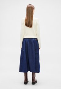 Denim maxi-rok met een elastische tailleband, zijzakken en een lichtblauwe wassing, gecombineerd met een crèmekleurige trui en bruine laarzen tot aan de knie.