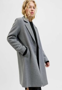 Manteau en mélange de laine gris avec un design ajusté, revers crantés et poches latérales. Présente une coupe décontractée et des poignets noirs côtelés en dessous.