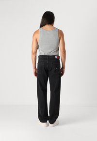 Tricou gri fără mâneci, blugi negri largi cu etichetă logo, buzunare din spate vizibile și o textură netedă, asortați cu adidași albi cu talpă joasă.