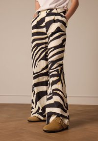 Wide-leg pants in a zebra print, featuring black and cream colors with gold accents. Made from lightweight fabric, with side pockets.