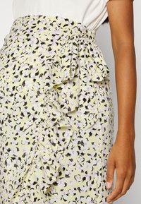 Rok met bloemenpatroon in geel met zwarte en lila accenten. Voorzien van ruches en een strikdetail aan de zijkant. Gemaakt van lichtgewicht stof.