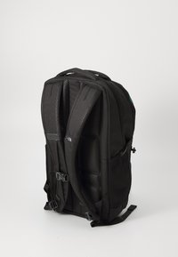Mochila negra con respaldo acolchado, bolsillos laterales de malla, correas ajustables y un asa superior. Presenta un diseño elegante y moderno, y está fabricada con un tejido duradero.