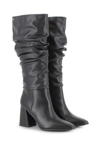 Botas negras de cuero, altas hasta la rodilla, con puntera afilada y tacones gruesos, sobre un fondo blanco.