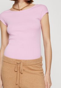 Pink fitted top with short sleeves, made of stretchy fabric. Paired with a light brown knit skirt featuring a tie waist.