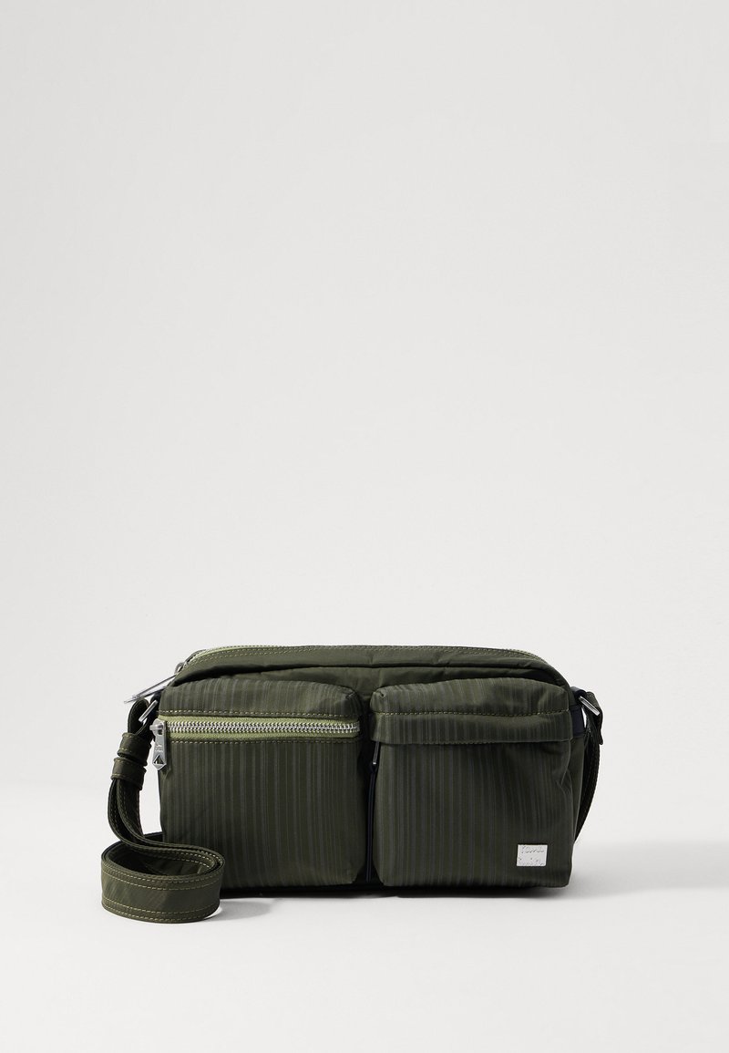 Oliven grønn nylon skulderveske med to frontlommer med glidelås, strukturerte striper og justerbar stropp. Sølvfarget hardware- detaljer.