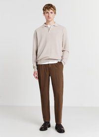 Pull en tricot beige à col polo superposé sur une chemise blanche, associé à un pantalon tailleur marron et des mocassins noirs. Design minimaliste, coupe décontractée.