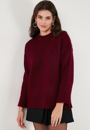 Suéter de punto burdeos con un escote de cuello redondo acanalado, mangas largas y dobladillo curvado. La tela parece suave y texturada para mayor comodidad.