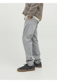 Pantaloni grigi su misura con taglio dritto, realizzati in un tessuto leggero, abbinati a sneaker nere con suole marroni.