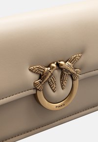 Pochette in pelle beige con una superficie liscia, caratterizzata da un ornato fermaglio ad anello in tonalità oro con due uccelli. Dettaglio di cucitura lungo i bordi.